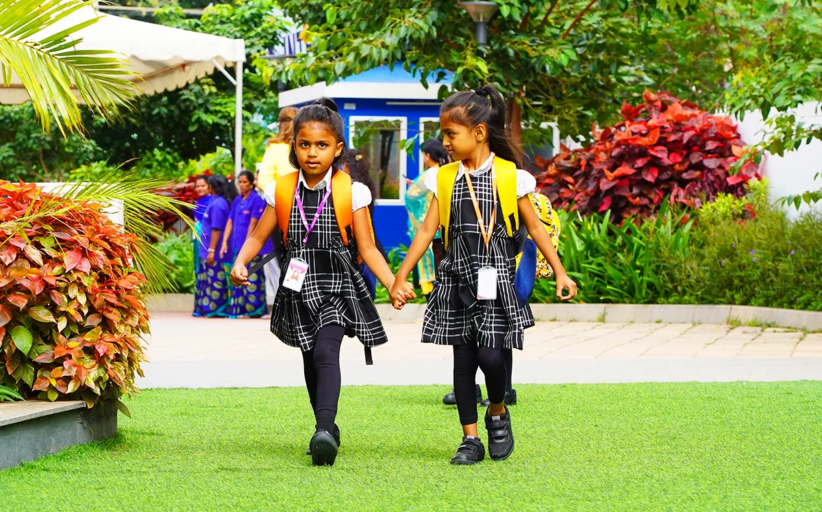 Two young learners walking hand in hand across the campus lawn
