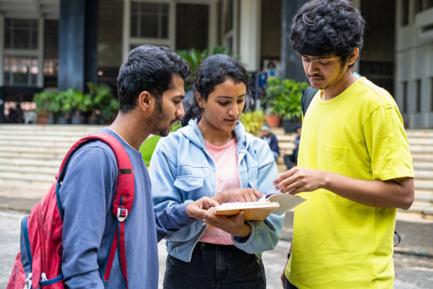 group of young indian Students busy on by discussing of syllabus during examination at college campus - concept of learning discussion and friendship
